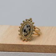 Gold ring with decorative lionfish design on a wooden block against a gray background
