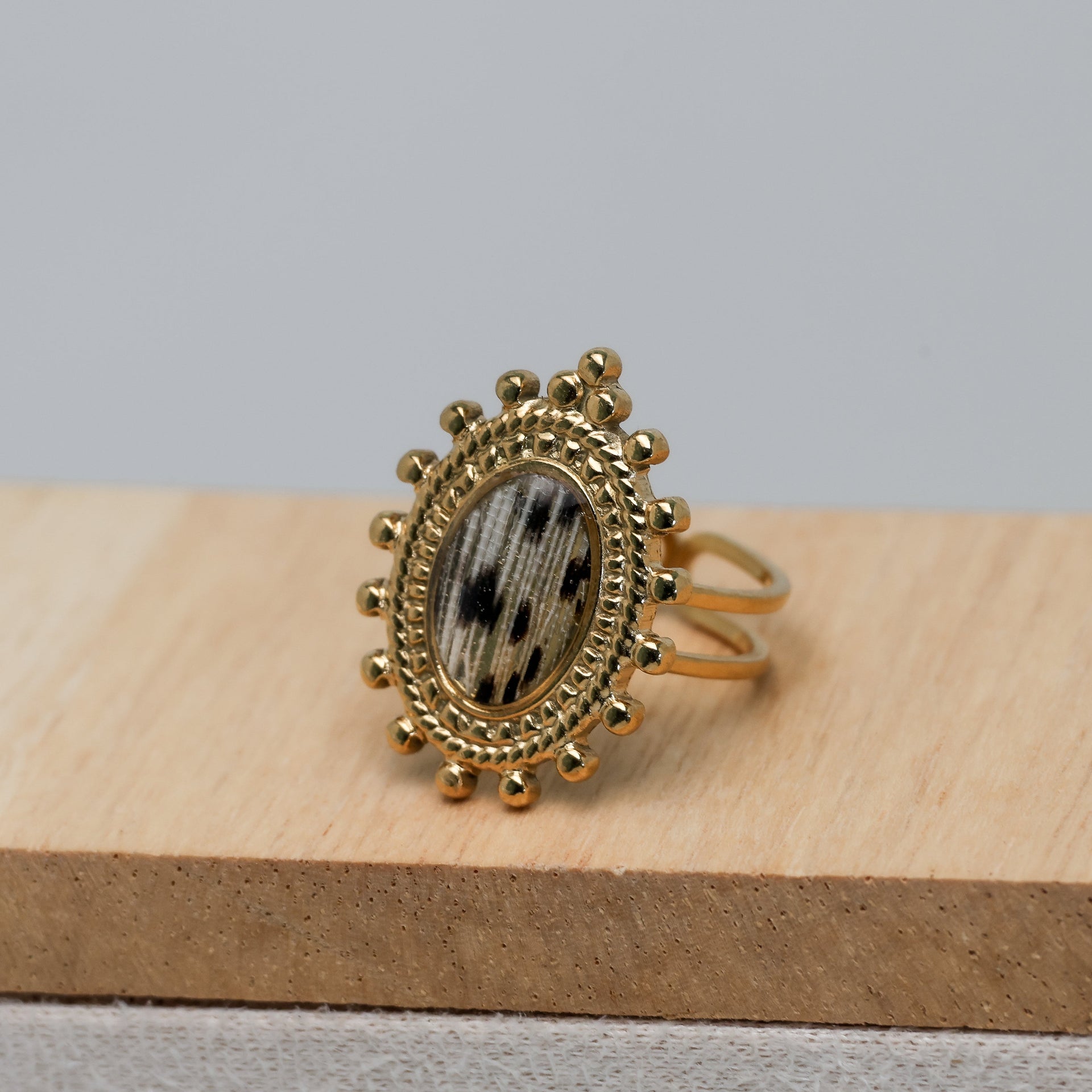 Gold ring with decorative lionfish design on a wooden block against a gray background