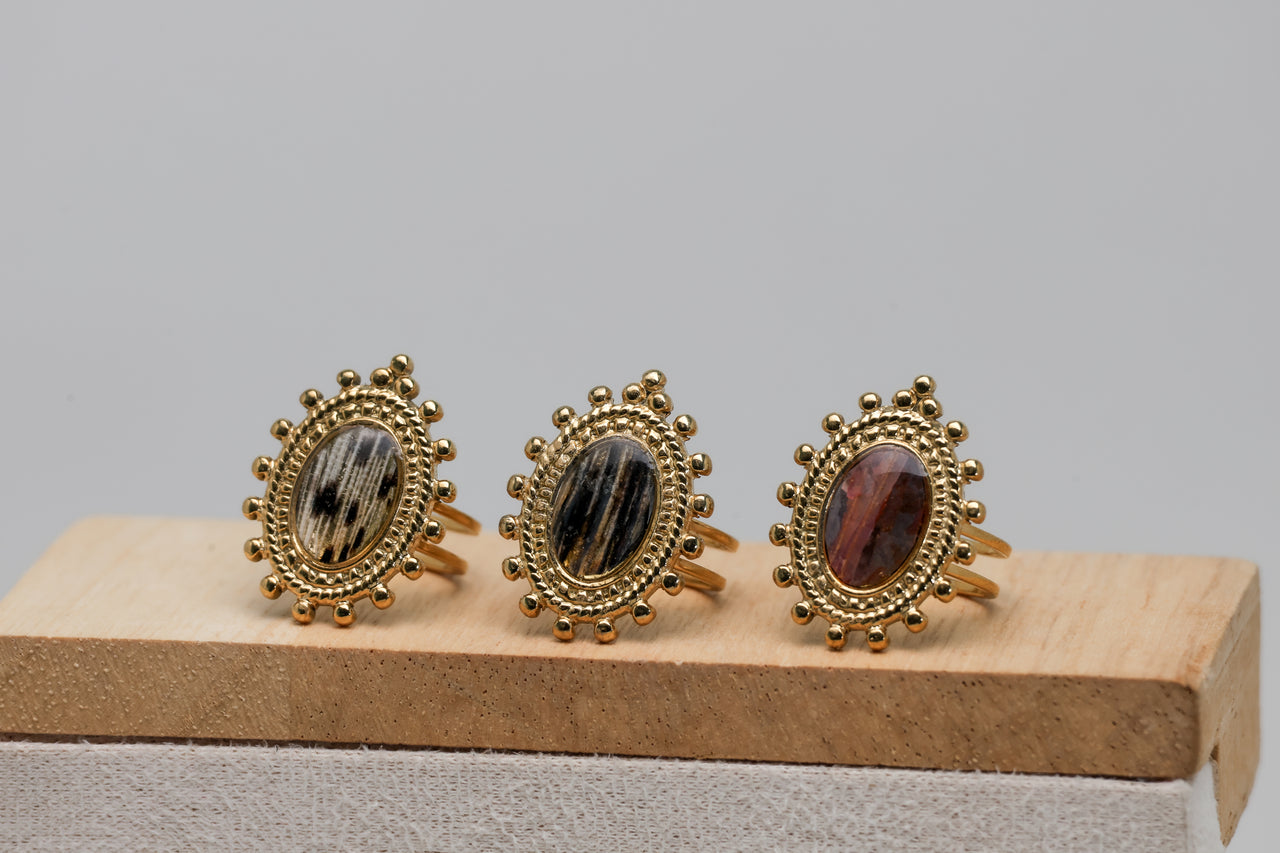 Three gold rings with lionfish fin gemstones on a wooden stand against a gray background