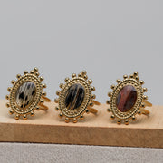 Three gold rings with lionfish fin gemstones on a wooden stand against a gray background