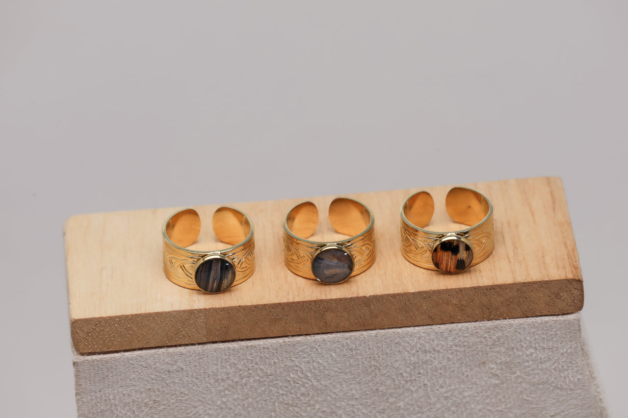 Three gold rings with embedded lionfish fins on a wooden stand against a gray background