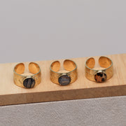 Three gold rings with embedded lionfish fins on a wooden stand against a gray background