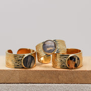 Gold rings with lionfish fin inlays on a wooden block against a gray background