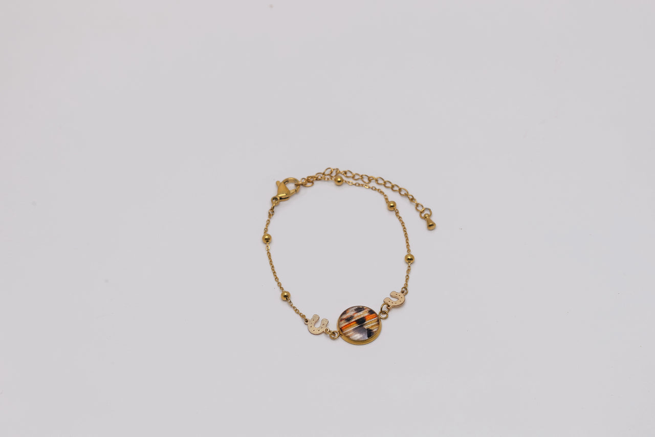 Gold bracelet with a colorful lionfish fin on a light gray background