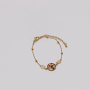 Gold bracelet with a colorful lionfish fin on a light gray background