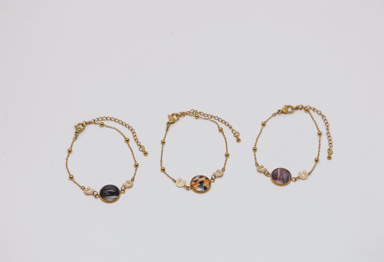 Three gold bracelets with lionfish fins on a light gray background