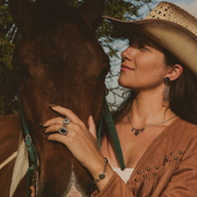 Woman in a cowboy hat petting a horse in a natural setting