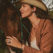 Woman in cowboy hat beside horse wearing lionfish jewelry, boot earrings, rings, and silver necklace
