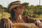 Woman in cowboy hat and leather jacket sitting on a horse in a desert landscape