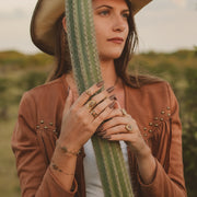 Woman in a cowboy hat and brown jacket holding a cactus in a natural setting