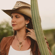 Woman in cowboy hat and leather jacket standing next to a cactus
