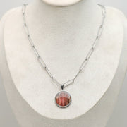A Large Silver Necklace on a cream necklace display bust. 