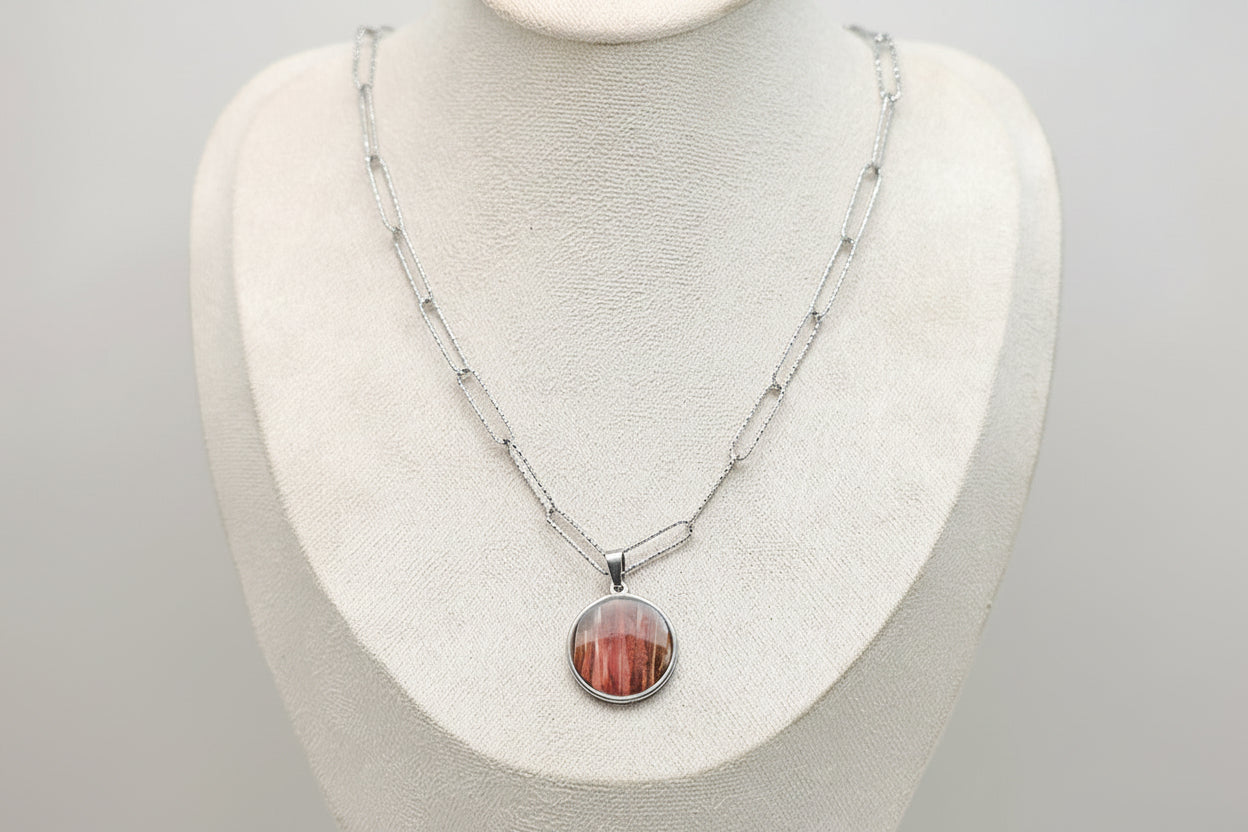 A Large Silver Necklace on a cream necklace display bust. 