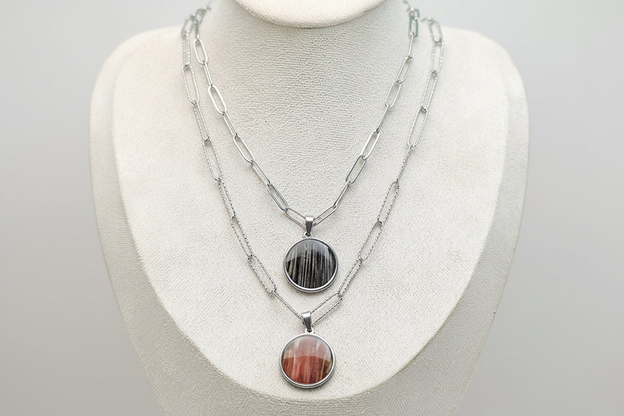 Two Large Silver Necklaces on a cream necklace display bust. 