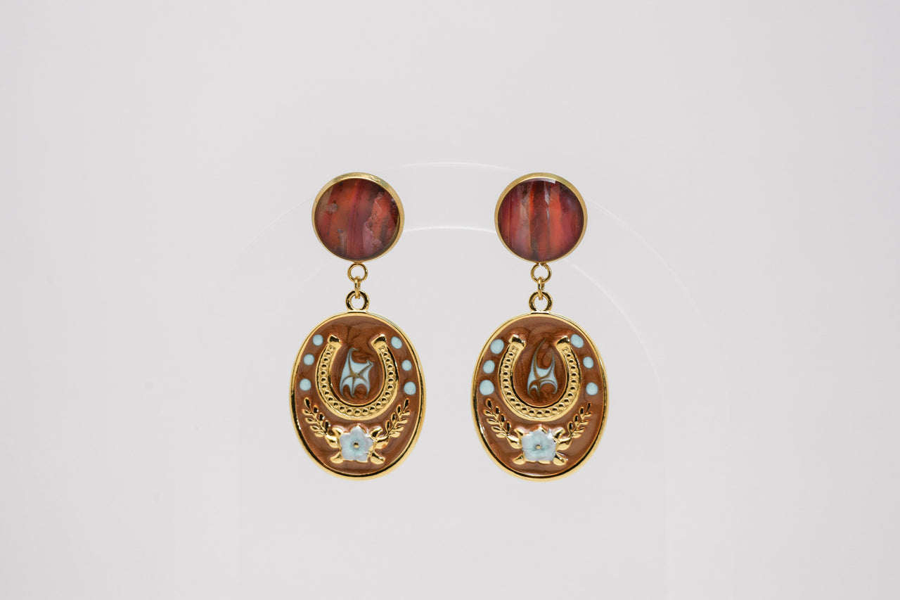 Pair of gold earrings with red lionfish fins and star designs on a light gray background