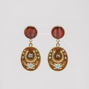 Pair of gold earrings with red lionfish fins and star designs on a light gray background