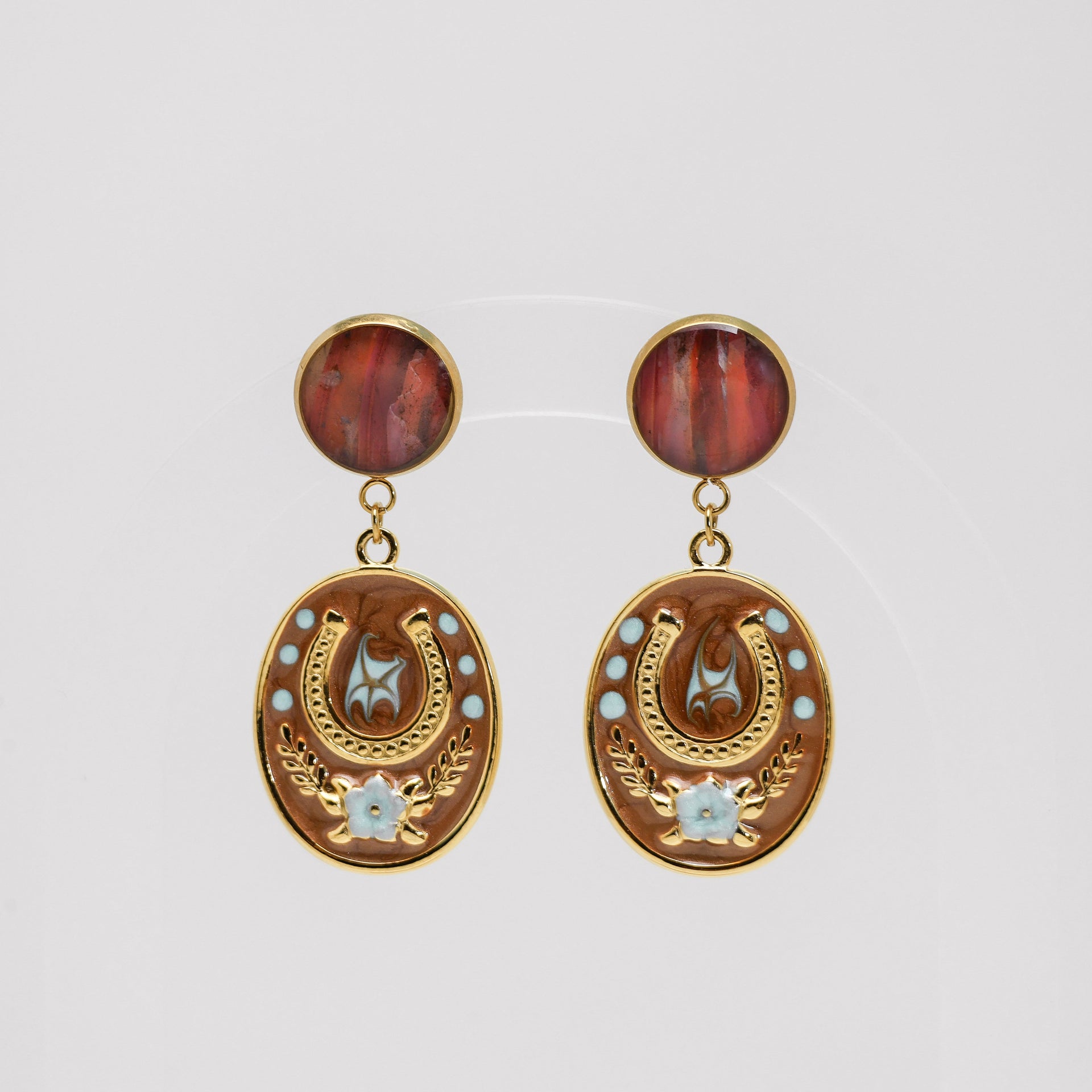 Pair of gold earrings with red lionfish fins and star designs on a light gray background