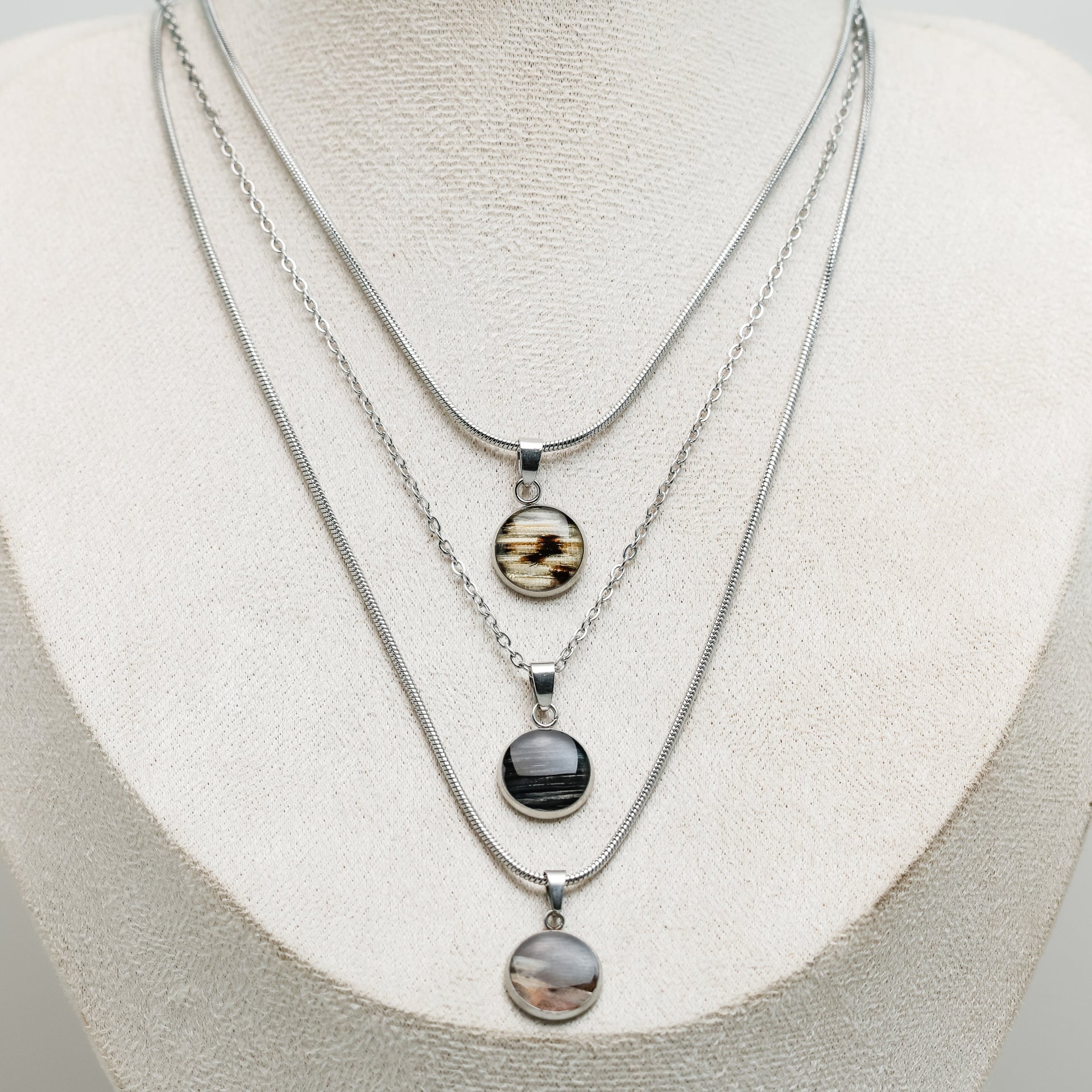 Three silver necklaces with pendant stones on a white mannequin bust.