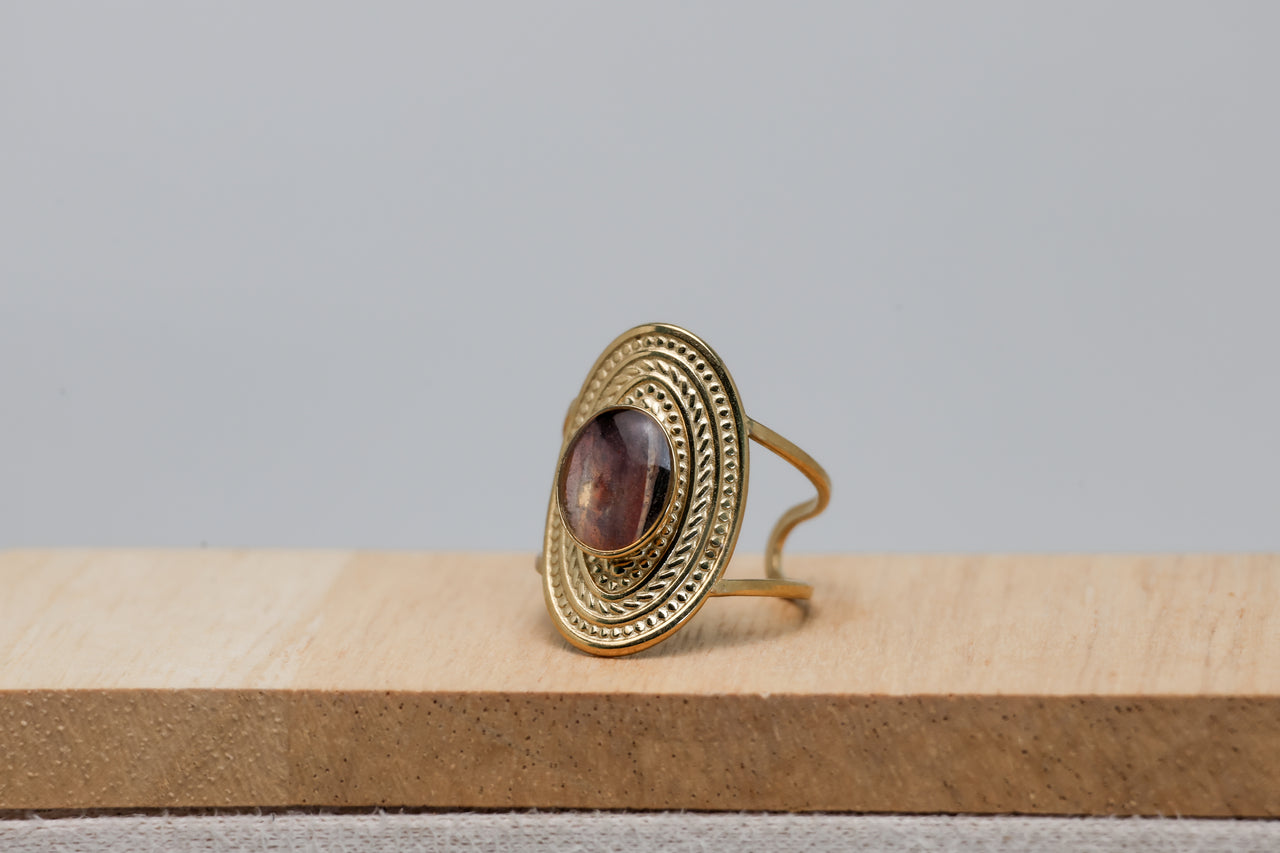Gold ring with a purple lionfish fin on a wooden surface with a gray background