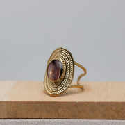 Gold ring with a purple lionfish fin on a wooden surface with a gray background