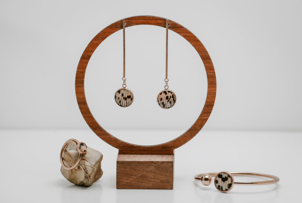 Rose gold Jewelry set including earrings, a bracelet cuff and a ring on a wooden stand with a white background