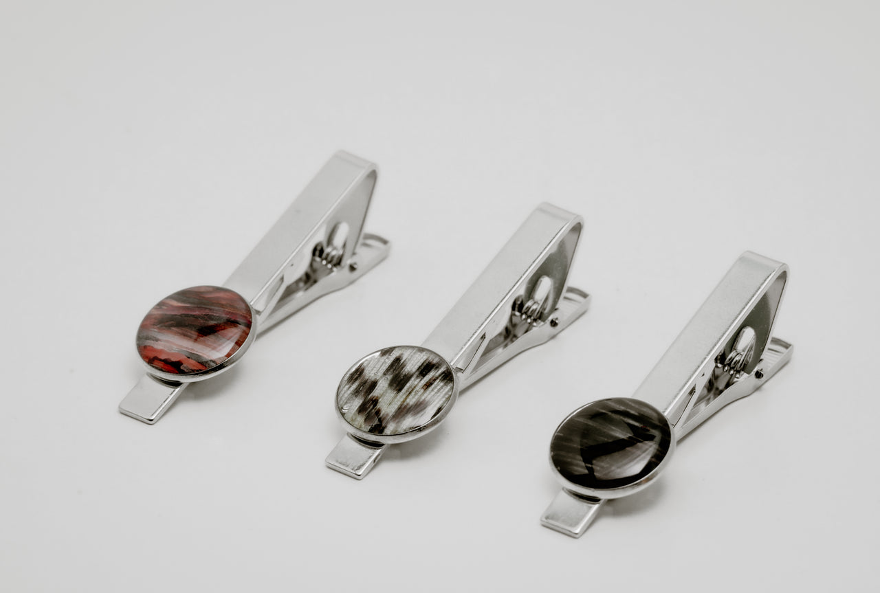Three silver tie clips with lionfish fin button on a light gray background