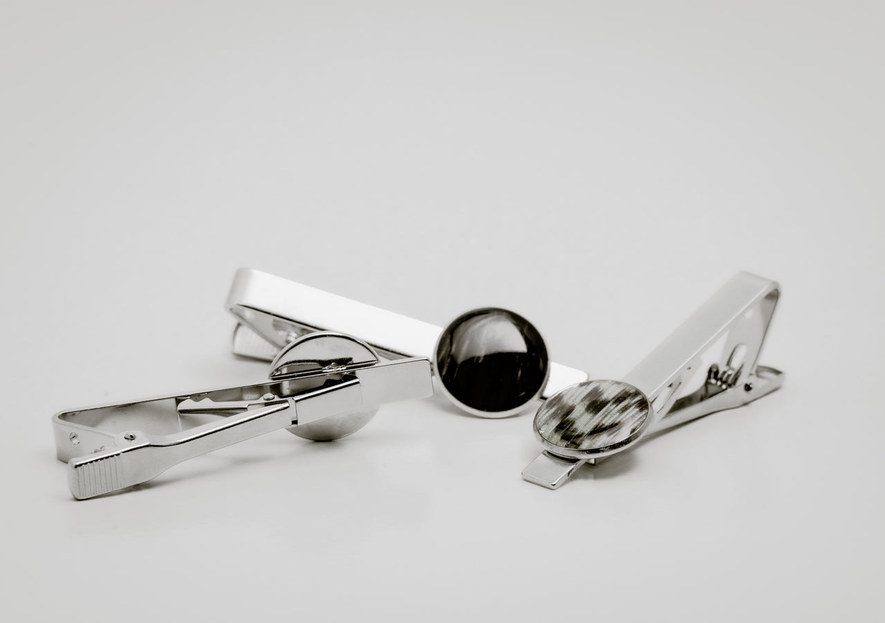Three silver tie clips with lionfish fin button on a light gray background