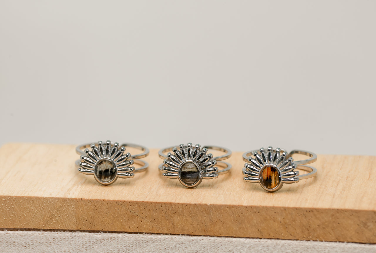 Three silver rings with lionfish fins on a wooden block against a gray background