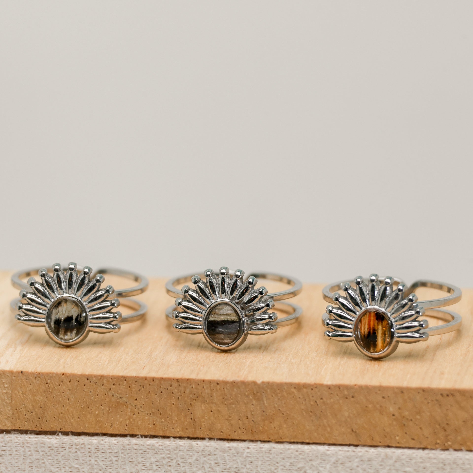 Three silver rings with lionfish fins on a wooden block against a gray background