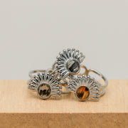 Three silver rings with sunburst design and lionfish fins on a wooden block.