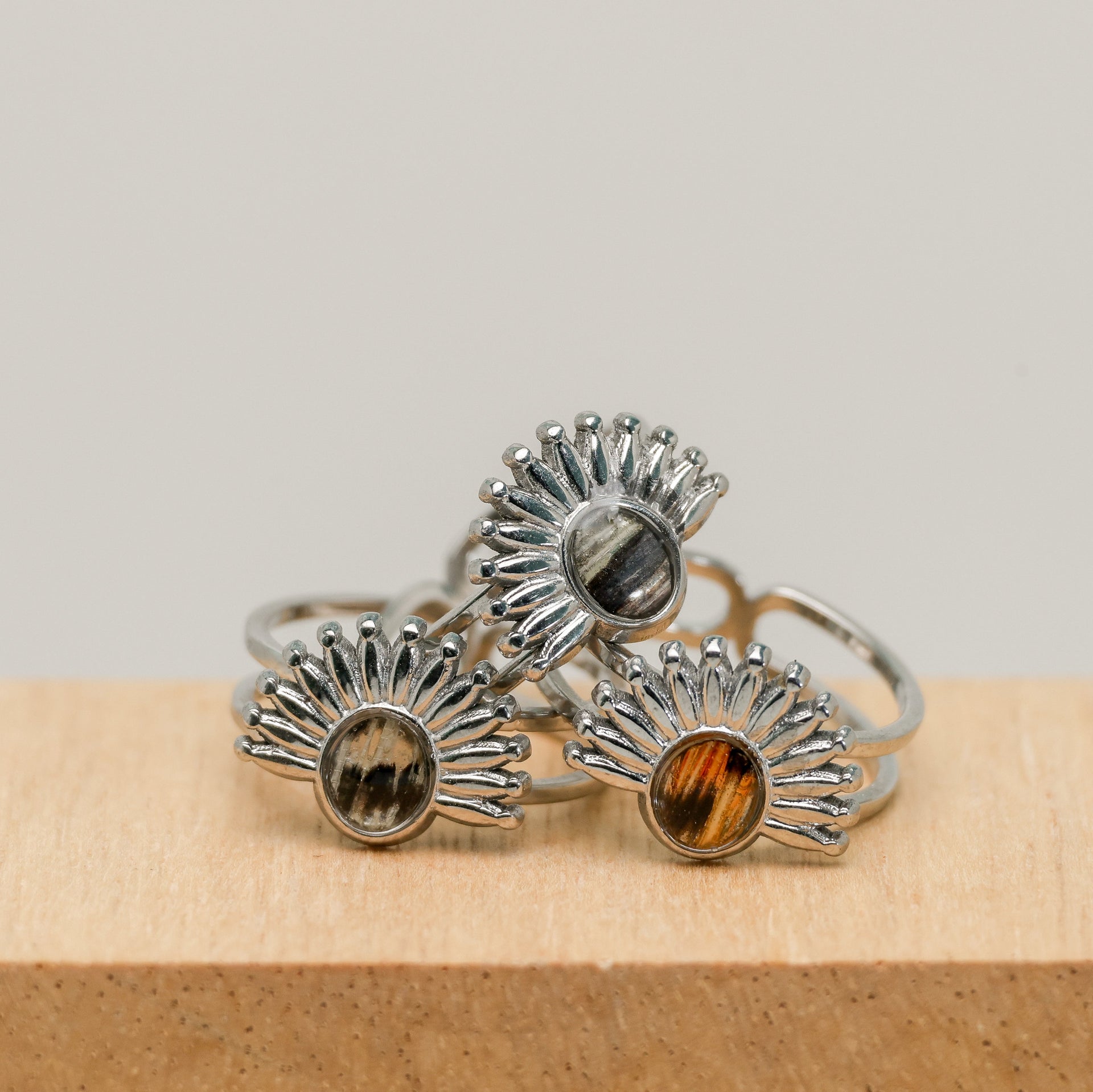 Three silver rings with sunburst design and lionfish fins on a wooden block.