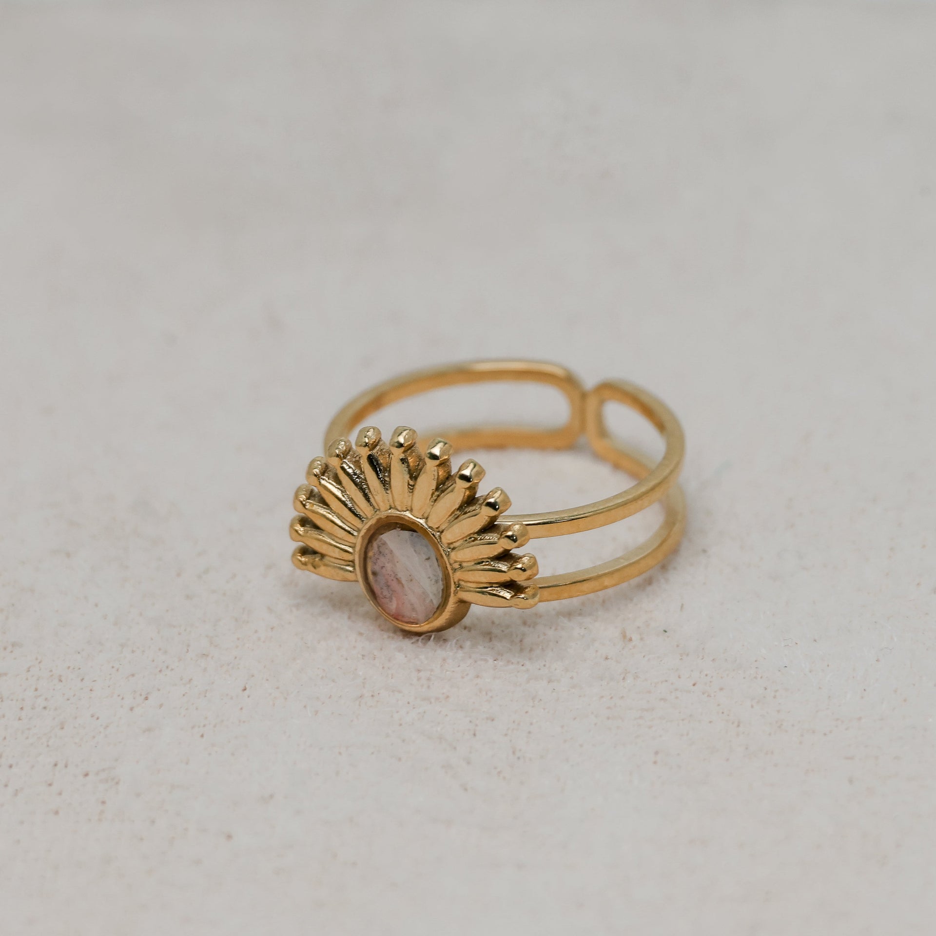 Gold ring with a pink lionfish fin on a light gray background