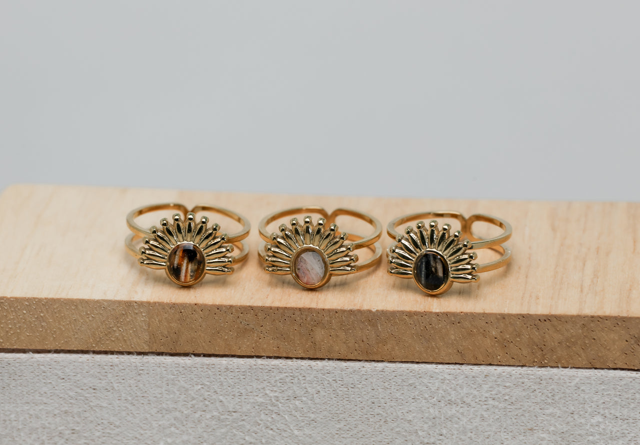 Three gold rings with different lionfish fins on a wooden block against a gray background