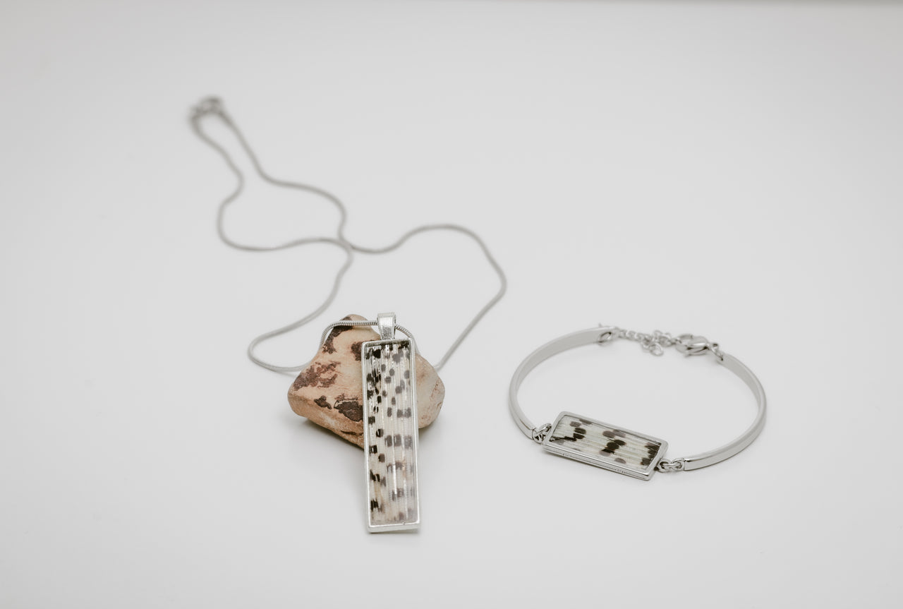 Silver necklace and bracelet with a lionfish fin pendant on a light gray background.