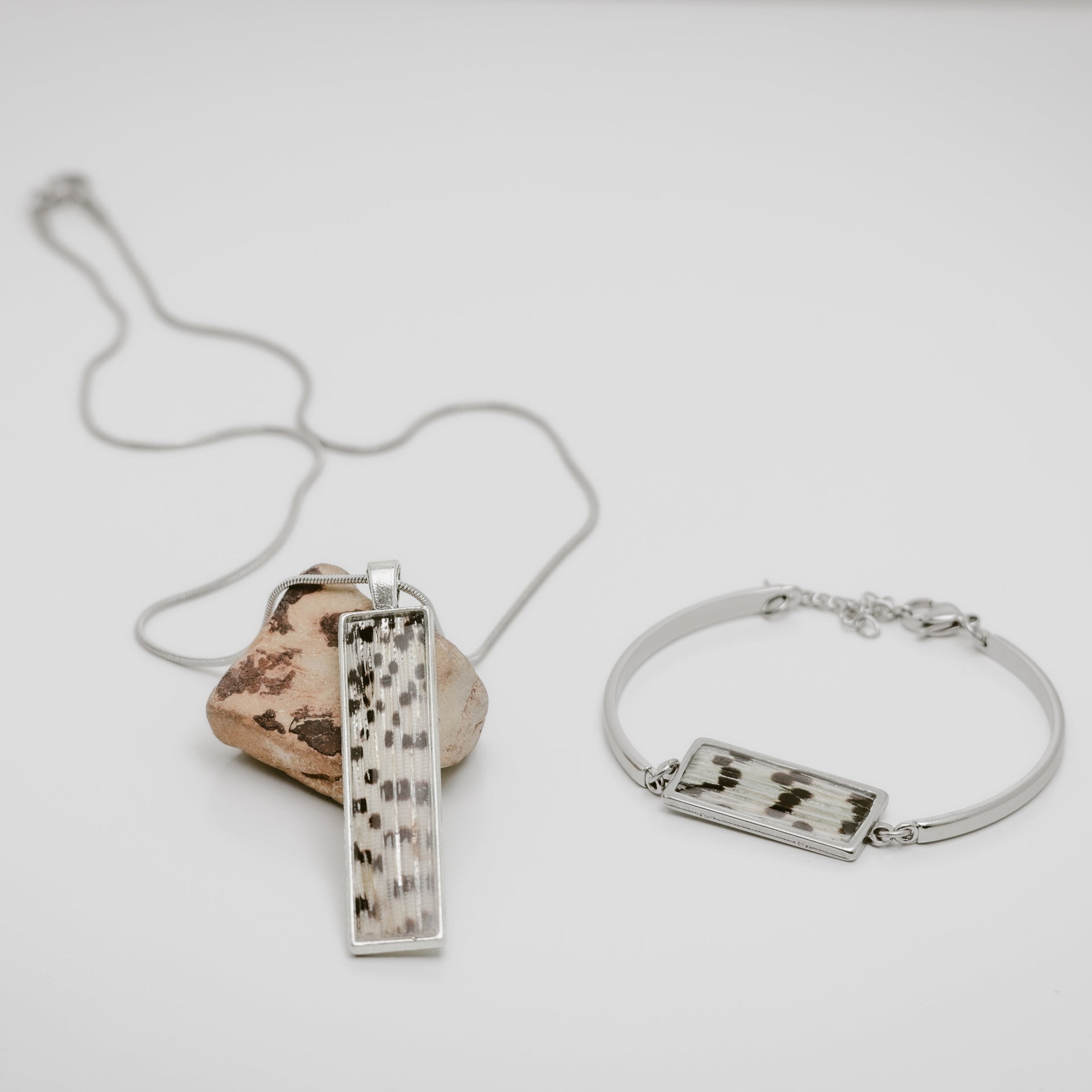 Silver necklace and bracelet with a lionfish fin pendant on a light gray background.