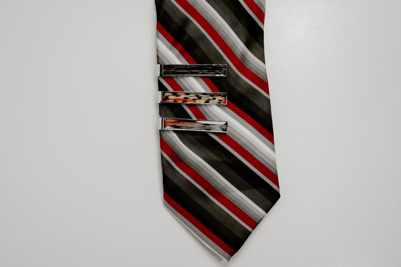 Striped tie with three tie clips on a light gray background