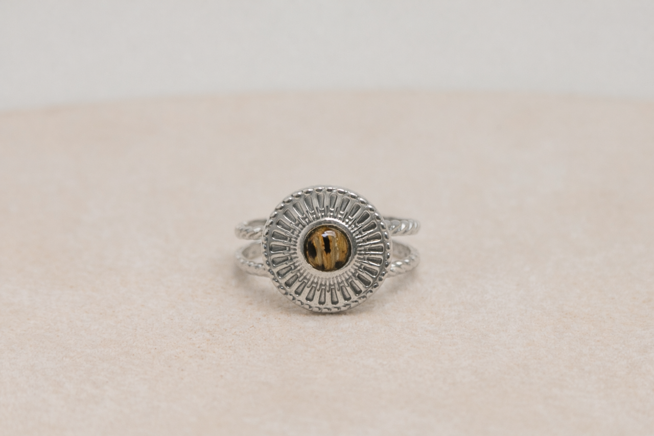 Silver ring with a circular lionfish design on a beige surface