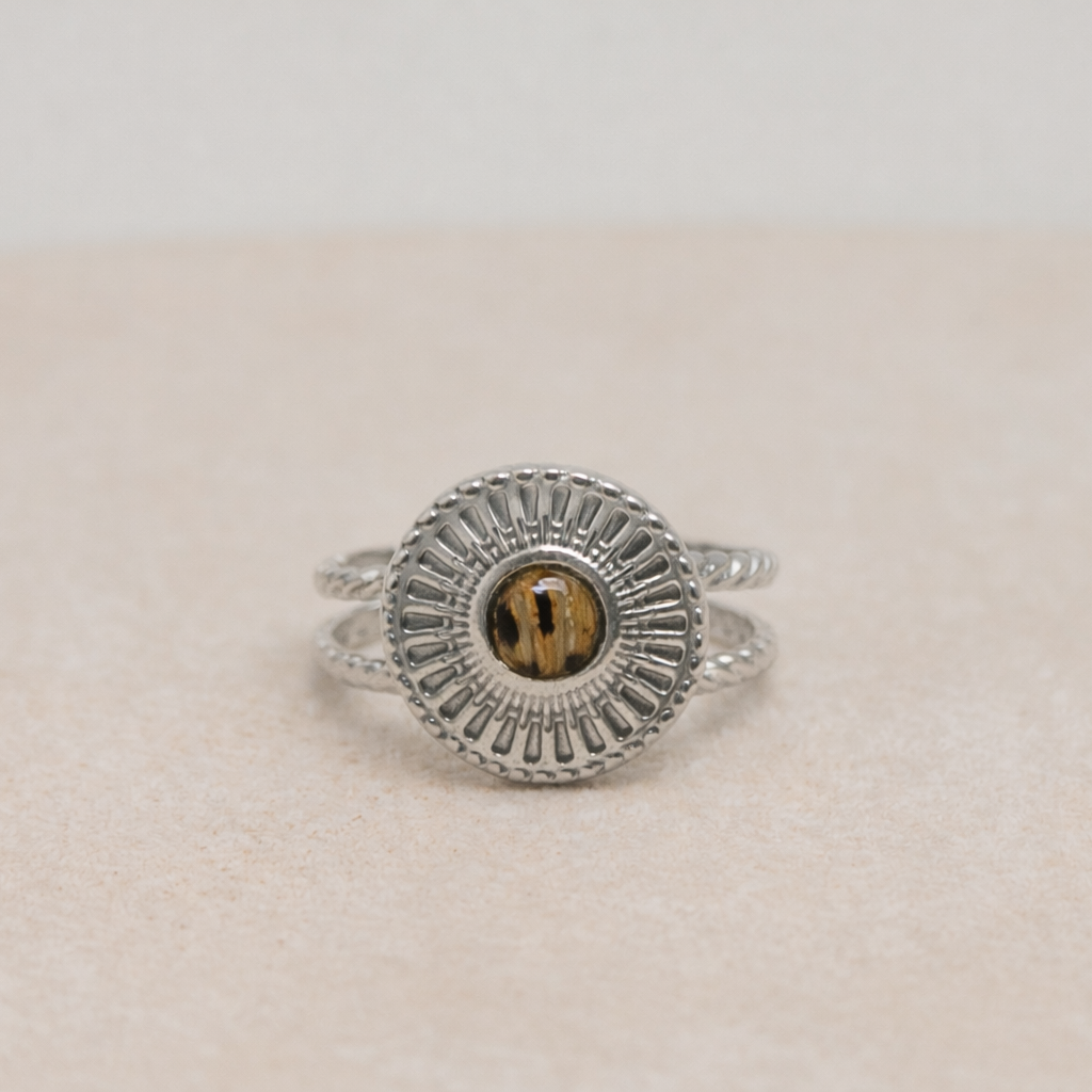 Silver ring with a circular lionfish design on a beige surface