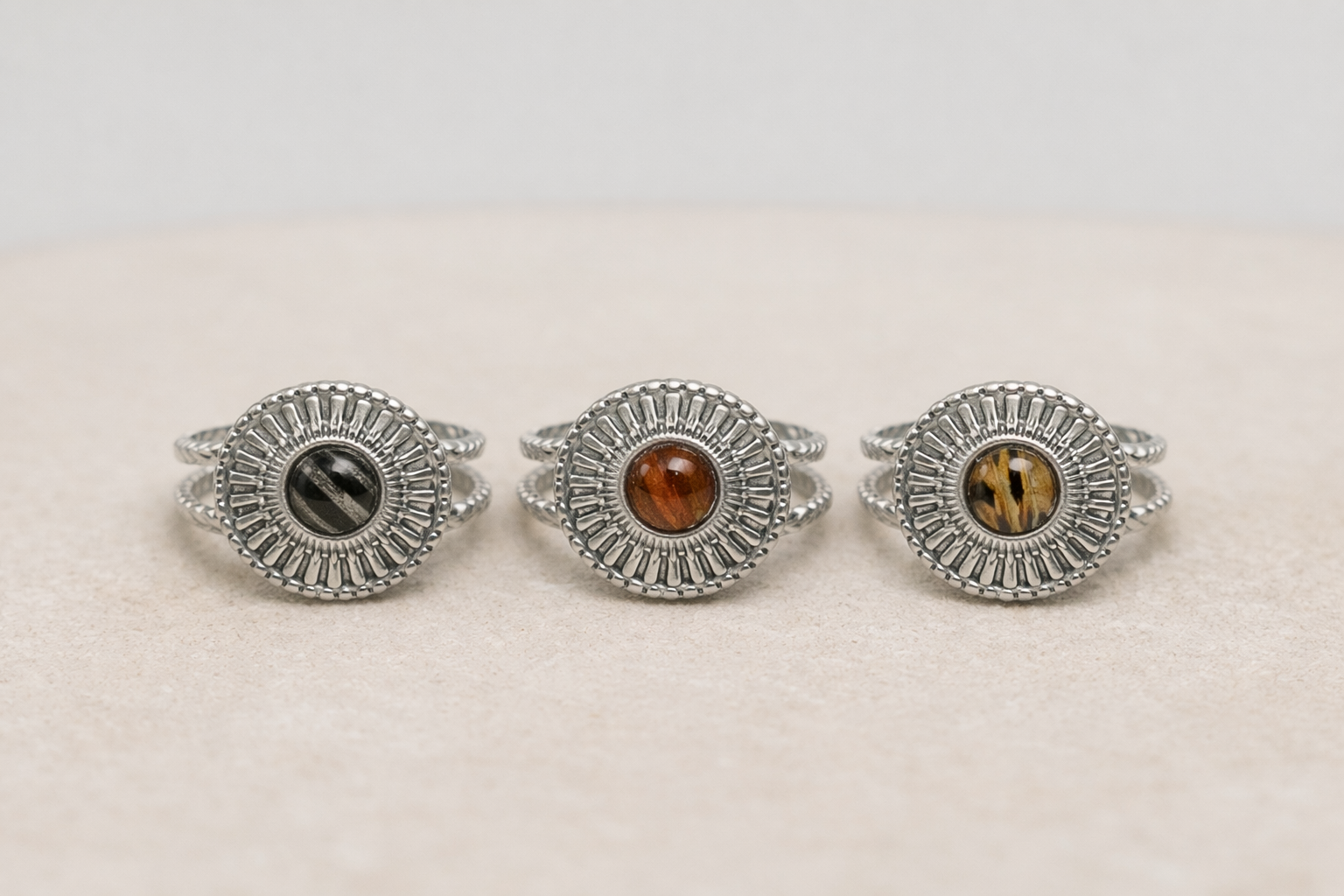 Three silver rings with embedded lionfish fins on a beige background