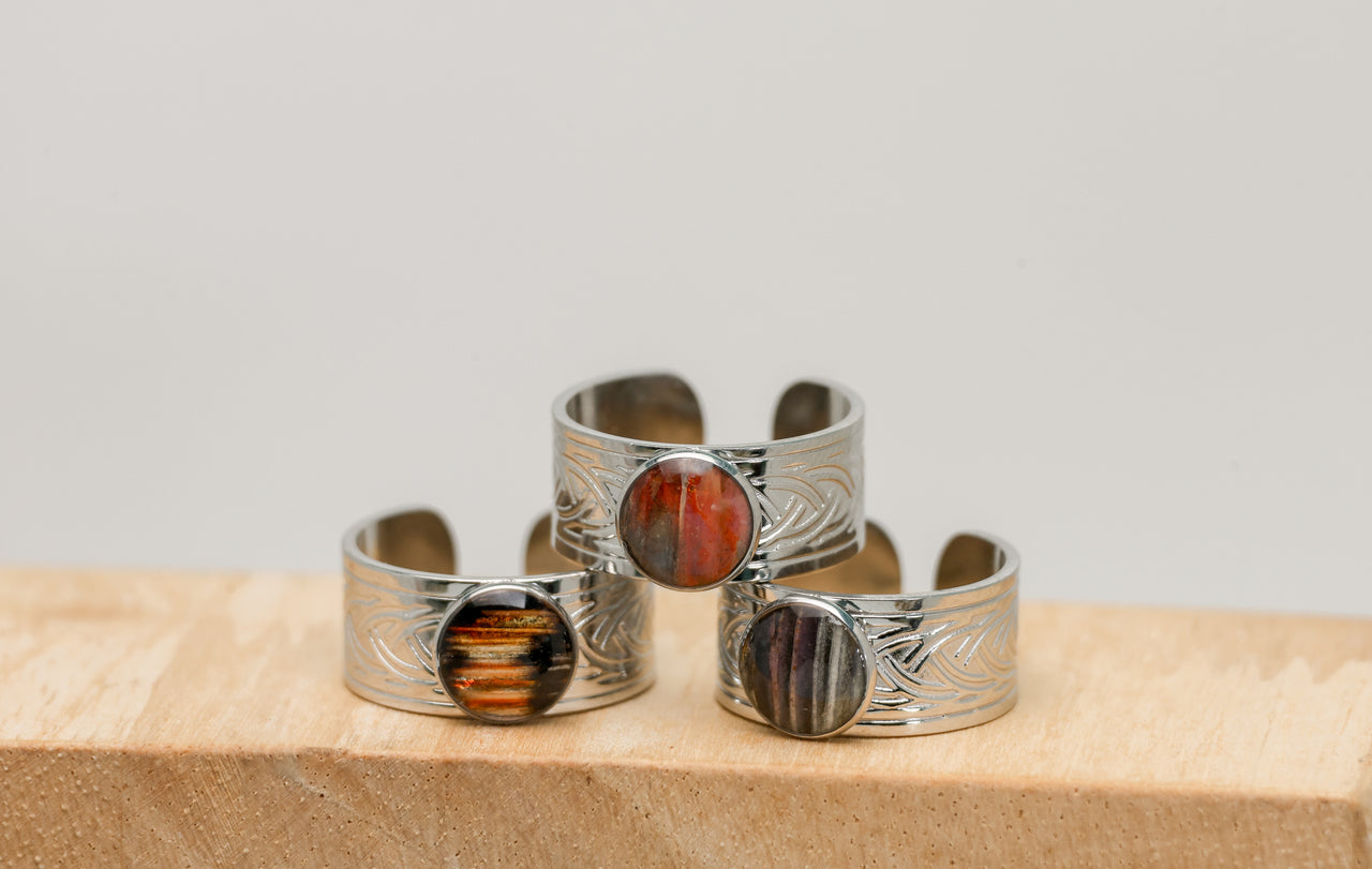 Three silver cuff bracelets with embedded lionfish fins on a wooden surface.