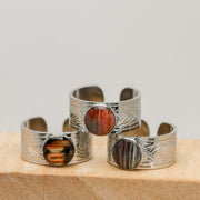 Three silver cuff bracelets with embedded lionfish fins on a wooden surface.