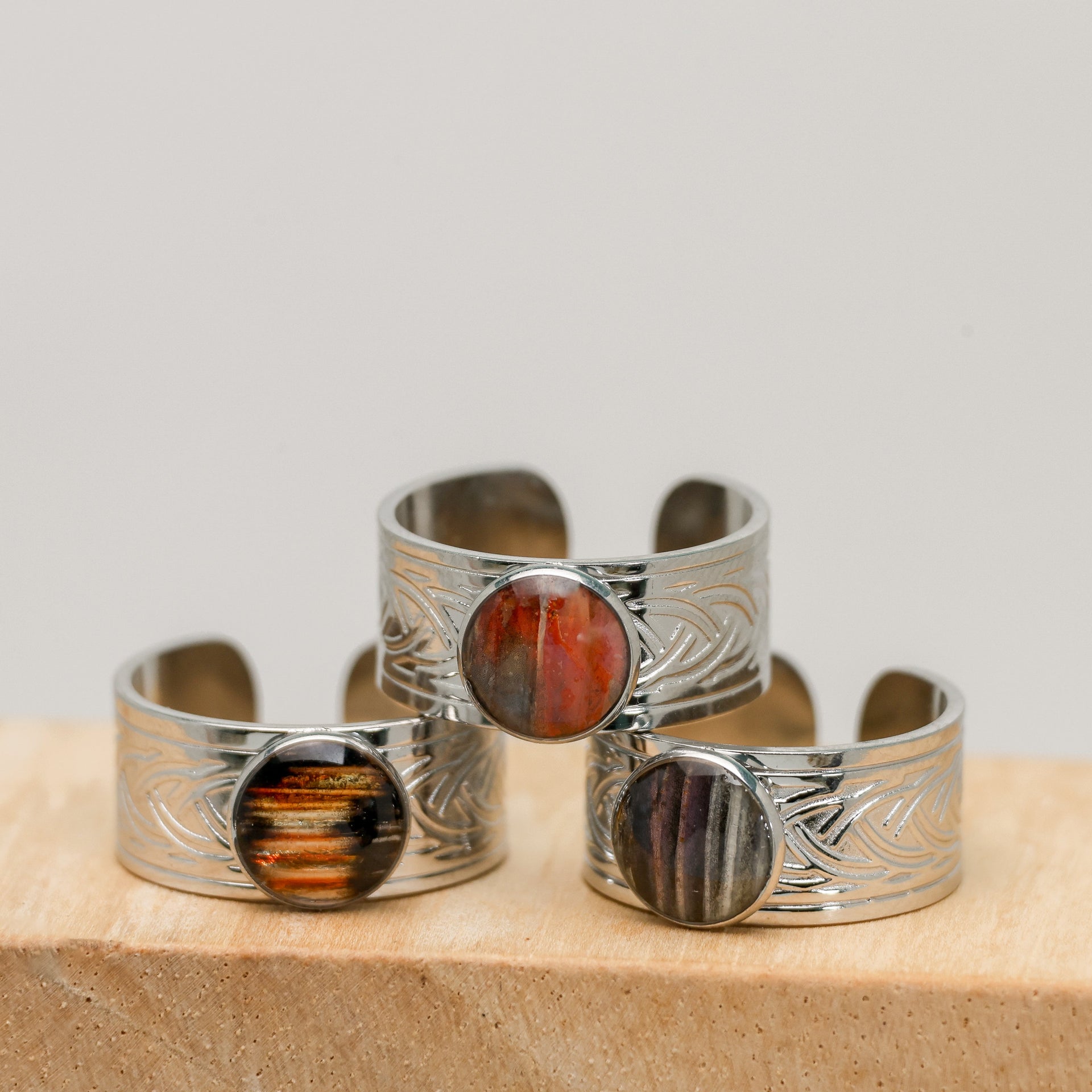 Three silver cuff bracelets with embedded lionfish fins on a wooden surface.