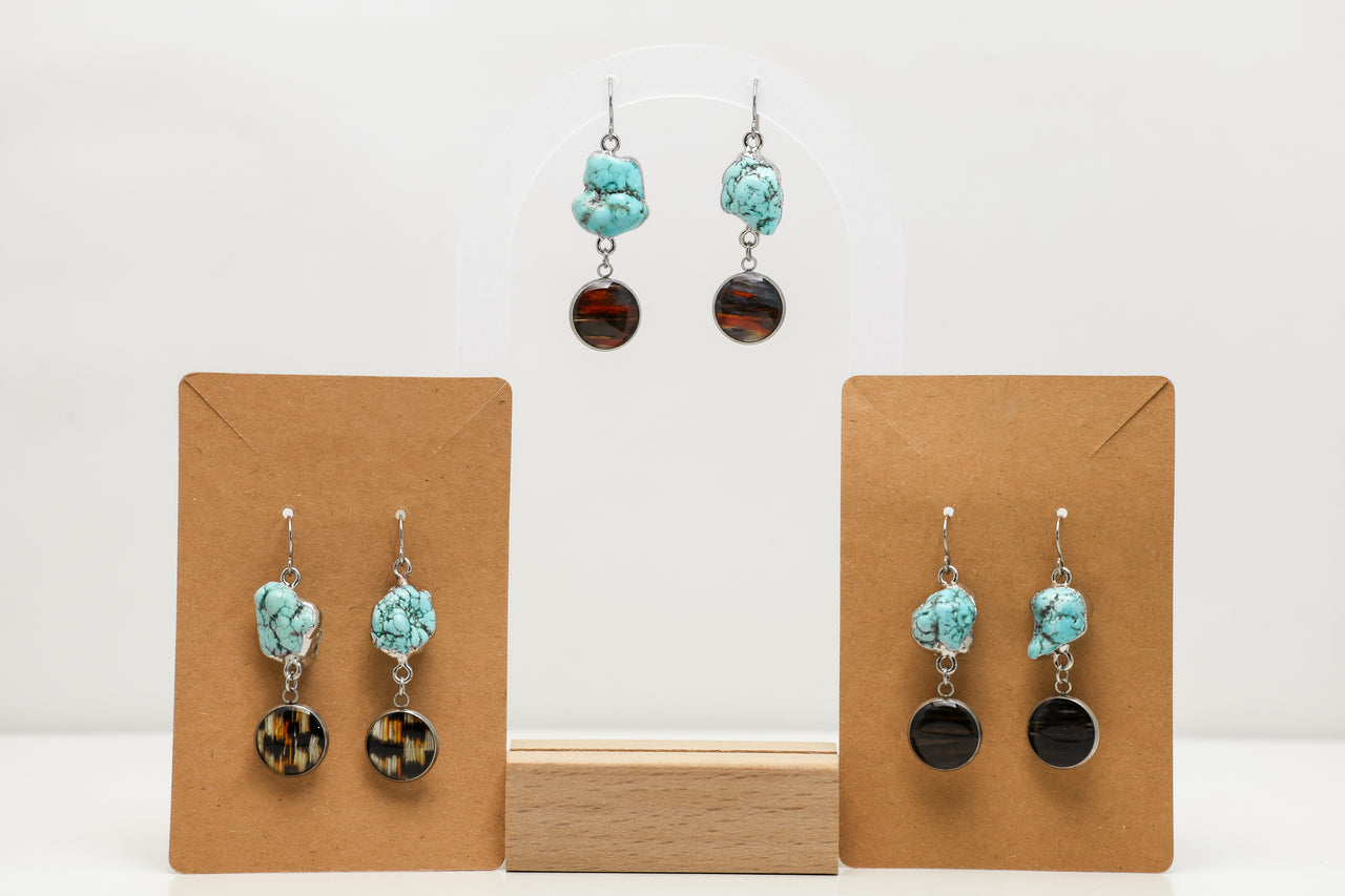 Turquoise and black lionfish earrings on wooden display stands against a white background