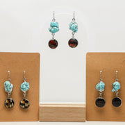 Turquoise and black lionfish earrings on wooden display stands against a white background