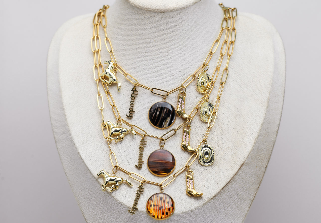 Gold necklace with various western and lionfish pendants on a mannequin bust against a gray background