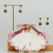 Two pairs of Petite Shell Earrings on stands on a white background.  A third pair is in a pink clam shell. 