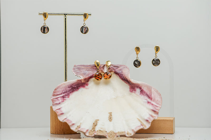 Two pairs of Petite Shell Earrings on stands on a white background.  A third pair is in a pink clam shell. 