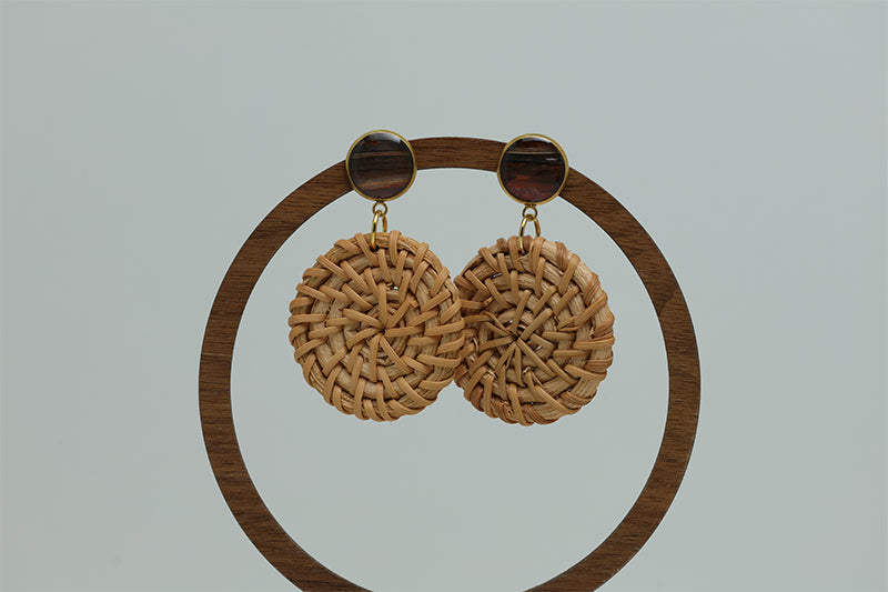 Boho Rattan Circular Earrings ion a circular wooden stand on a gray background.  