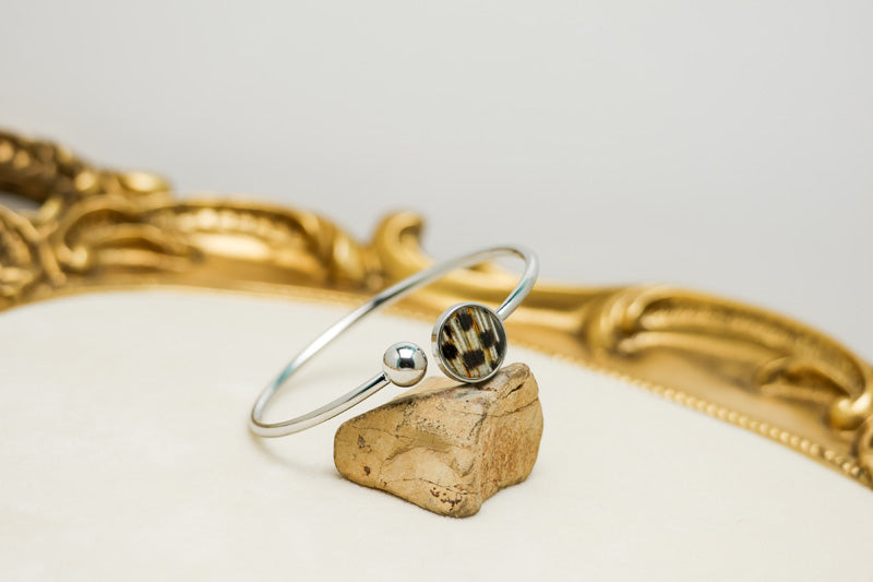  A Silver Cuff on a rock on a white background with gold frame. 