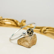  A Silver Cuff on a rock on a white background with gold frame. 